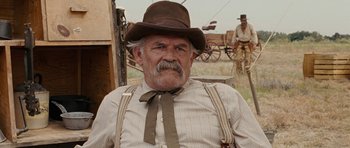 Movie still from “True Grit” (2010), directed by Ethan Coen – An older man with a mustache wearing a brown hat; Close Up shot, Over the shoulder angle