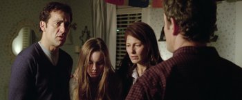 Movie still from “Trust” (2010), directed by David Schwimmer – Two women and a man are standing in a living room; Medium shot, Over the shoulder angle