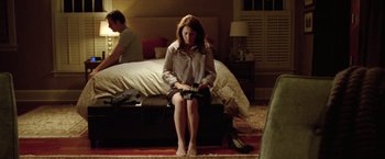 Movie still from “Trust” (2010), directed by David Schwimmer – A woman sitting on a bed with a man sitting on the bed in the background; Wide shot, High angle
