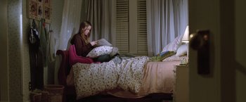 Movie still from “Trust” (2010), directed by David Schwimmer – A woman sitting on a bed reading a book; Wide shot, High angle
