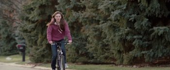 Movie still from “Trust” (2010), directed by David Schwimmer – A woman riding a bike down a road near a forest; Wide shot, Over the shoulder angle