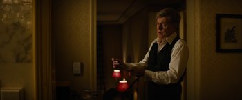 Movie still from “Truth” (2015), directed by James Vanderbilt – An older man in a white shirt and black vest holding a red lamp; Medium shot, Over the shoulder angle