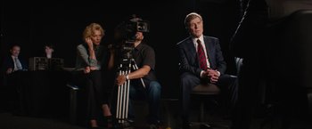 Movie still from “Truth” (2015), directed by James Vanderbilt – A man sitting on top of a chair next to two women; Medium shot, Over the shoulder angle
