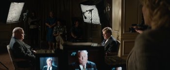 Movie still from “Truth” (2015), directed by James Vanderbilt – A man sitting in a chair in front of a video camera; Medium shot, Over the shoulder angle