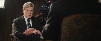 Movie still from “Truth” (2015), directed by James Vanderbilt – A man wearing a suit and tie sitting in front of a camera; Close Up shot, Over the shoulder angle