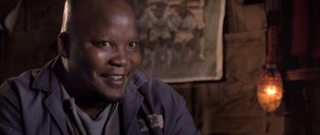 Movie still from “Tsotsi” (2005), directed by Gavin Hood – A person sitting in front of a painting; Close Up shot, Low angle