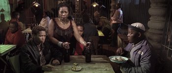Movie still from “Tsotsi” (2005), directed by Gavin Hood – A woman is pouring a drink at a restaurant; Medium shot, Over the shoulder angle