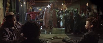 Movie still from “Tsotsi” (2005), directed by Gavin Hood – A man standing in front of a crowd of people in a room; Medium shot, Over the shoulder angle