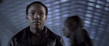 Movie still from “Tsotsi” (2005), directed by Gavin Hood – A man wearing a leather jacket standing in front of a window; Close Up shot, Low angle