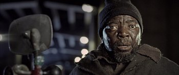 Movie still from “Tsotsi” (2005), directed by Gavin Hood – A person wearing a hat and a coat; Close Up shot, Low angle