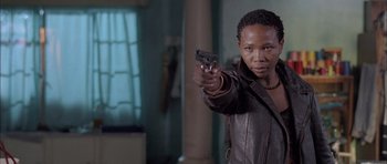 Movie still from “Tsotsi” (2005), directed by Gavin Hood – A woman holding a gun while wearing a leather jacket; Medium shot, Low angle