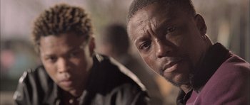 Movie still from “Tsotsi” (2005), directed by Gavin Hood – A man in a black jacket is looking at the camera; Close Up shot, Low angle