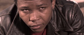 Movie still from “Tsotsi” (2005), directed by Gavin Hood – A person wearing a leather jacket; Close Up shot, Low angle