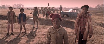 Movie still from “Tsotsi” (2005), directed by Gavin Hood – A group of people standing in a dirt field; Medium shot, Low angle