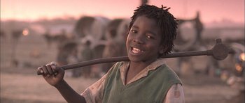 Movie still from “Tsotsi” (2005), directed by Gavin Hood – A young boy is smiling while holding a stick; Close Up shot, Low angle