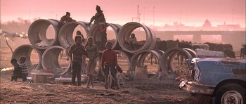 Movie still from “Tsotsi” (2005), directed by Gavin Hood – A group of people standing next to a bunch of pipes; Wide shot, Low angle