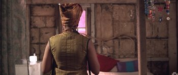 Movie still from “Tsotsi” (2005), directed by Gavin Hood – A person wearing a hood and a vest in front of a window; Medium shot, Over the shoulder angle