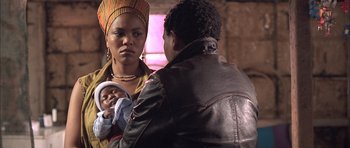 Movie still from “Tsotsi” (2005), directed by Gavin Hood – A woman holding a baby in her arms while standing next to a man in a leather jacket; Close Up shot, Over the shoulder angle