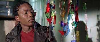 Movie still from “Tsotsi” (2005), directed by Gavin Hood – A woman standing in front of a window with many glass ornaments hanging from the ceiling; Close Up shot, Low angle