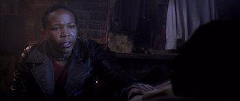 Movie still from “Tsotsi” (2005), directed by Gavin Hood – A man wearing a leather jacket sitting in a room; Close Up shot, Over the shoulder angle