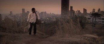Movie still from “Tsotsi” (2005), directed by Gavin Hood – A man standing on top of a hill near tall buildings; Wide shot, Low angle
