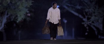 Movie still from “Tsotsi” (2005), directed by Gavin Hood – A man walking down a street holding two bags; Medium shot, Low angle