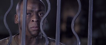 Movie still from “Tsotsi” (2005), directed by Gavin Hood – A person behind a metal fence; Close Up shot, High angle