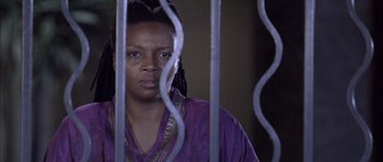 Movie still from “Tsotsi” (2005), directed by Gavin Hood – A woman in a purple shirt behind a metal fence; Close Up shot, Low angle
