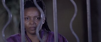Movie still from “Tsotsi” (2005), directed by Gavin Hood – A woman in a purple shirt is behind bars; Close Up shot, Low angle