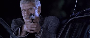 Movie still from “Tsotsi” (2005), directed by Gavin Hood – A man holding a gun while wearing a suit and tie; Close Up shot, Low angle