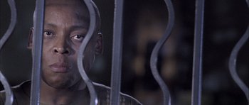 Movie still from “Tsotsi” (2005), directed by Gavin Hood – A person behind a metal fence; Close Up shot, Low angle