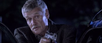 Movie still from “Tsotsi” (2005), directed by Gavin Hood – An older man holding a gun while wearing a jacket; Close Up shot, High angle