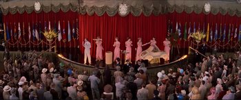 Movie still from “Tucker: The Man and His Dream” (1988), directed by Francis Ford Coppola – A group of people on a stage with a clock in the background; Wide shot, High angle