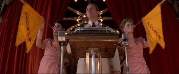 Movie still from “Tucker: The Man and His Dream” (1988), directed by Francis Ford Coppola – A man standing at a podium in front of two other people; Medium shot, Low angle