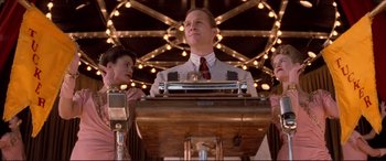 Movie still from “Tucker: The Man and His Dream” (1988), directed by Francis Ford Coppola – A man standing at a podium in front of a woman; Medium shot, Low angle