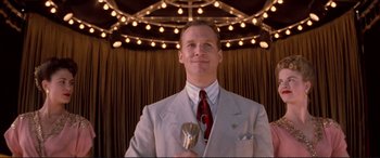 Movie still from “Tucker: The Man and His Dream” (1988), directed by Francis Ford Coppola – A man in a suit and tie holding a microphone in front of lights; Medium shot, Low angle