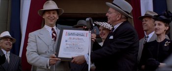 Movie still from “Tucker: The Man and His Dream” (1988), directed by Francis Ford Coppola – A man in a hat is holding up a certificate of completion; Medium shot, Low angle
