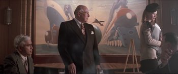 Movie still from “Tucker: The Man and His Dream” (1988), directed by Francis Ford Coppola – An older man in a suit standing in front of a painting; Medium shot, Low angle