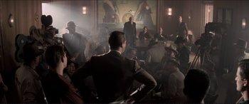 Movie still from “Tucker: The Man and His Dream” (1988), directed by Francis Ford Coppola – A group of people sitting in a room with a man standing in front of them; Wide shot, High angle