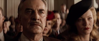 Movie still from “Tucker: The Man and His Dream” (1988), directed by Francis Ford Coppola – An older man looks at the camera while people watch; Close Up shot, Low angle