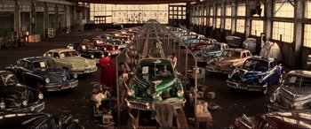 Movie still from “Tucker: The Man and His Dream” (1988), directed by Francis Ford Coppola – A group of men working on a car in a garage; Extreme Wide shot, High angle