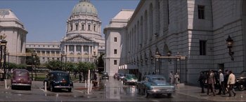 Movie still from “Tucker: The Man and His Dream” (1988), directed by Francis Ford Coppola – Cars are parked on the side of the street in front of a large building; Extreme Wide shot, High angle