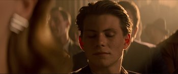 Movie still from “Tucker: The Man and His Dream” (1988), directed by Francis Ford Coppola – A young man with his eyes closed in a dimly - lit room; Close Up shot, Over the shoulder angle