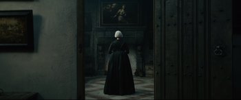 Movie still from “Tulip Fever” (2017), directed by Justin Chadwick – A woman in a black dress standing in front of a fireplace; Wide shot, Over the shoulder angle