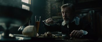 Movie still from “Tulip Fever” (2017), directed by Justin Chadwick – A man sitting at a table with a knife and a fork; Medium shot, Over the shoulder angle
