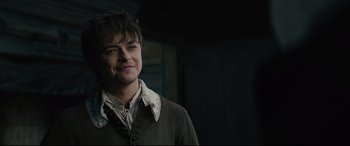 Movie still from “Tulip Fever” (2017), directed by Justin Chadwick – A man in a brown jacket smiling for the camera; Close Up shot, Over the shoulder angle