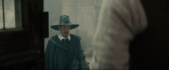 Movie still from “Tulip Fever” (2017), directed by Justin Chadwick – A man wearing a hat and a long coat; Medium shot, Over the shoulder angle
