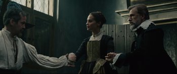 Movie still from “Tulip Fever” (2017), directed by Justin Chadwick – A young woman in a medieval dress holding hands with two men; Medium shot, Over the shoulder angle