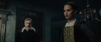Movie still from “Tulip Fever” (2017), directed by Justin Chadwick – A woman standing in front of a painting in a dark room; Medium shot, Over the shoulder angle