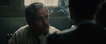 Movie still from “Tulip Fever” (2017), directed by Justin Chadwick – A man with a beard smoking a cigarette in front of another man; Close Up shot, Over the shoulder angle